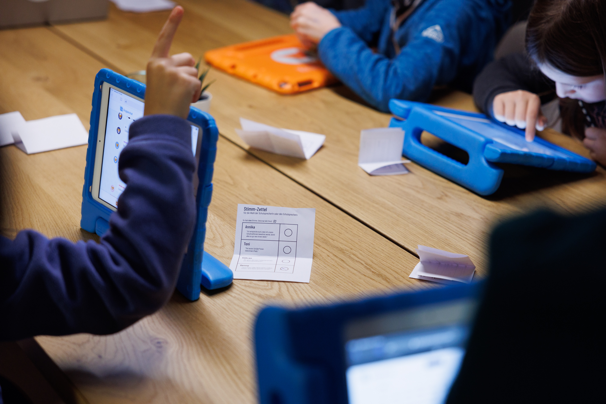 Kinder benutzen das Tablet. Auf dem Tisch davor liegen die Stimmzettel.